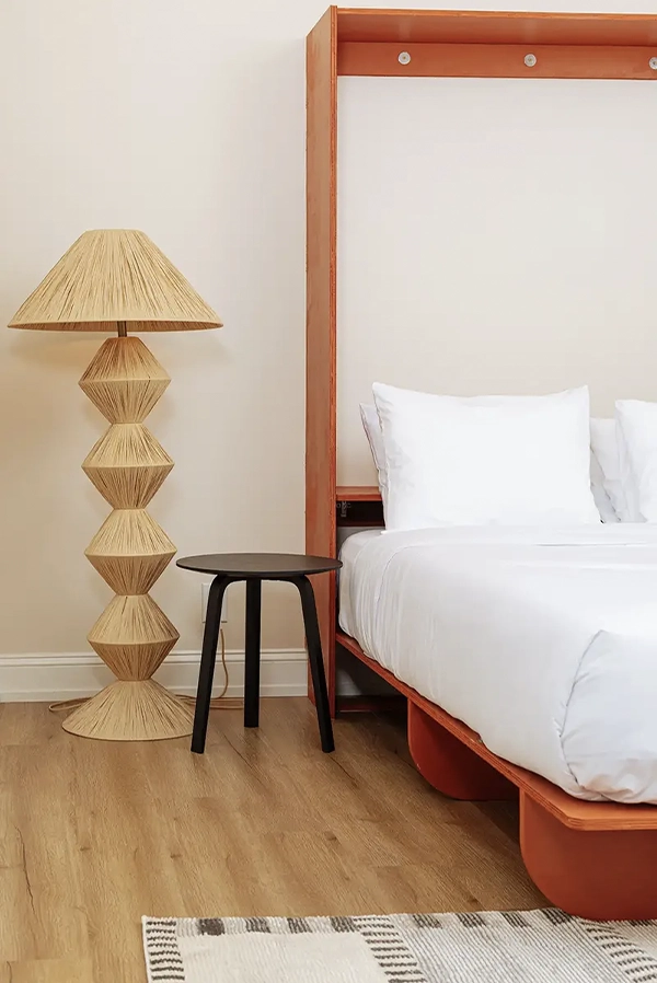 bedroom with double bed and withe bed sheets, a wooden floor lamp and a night table next to it