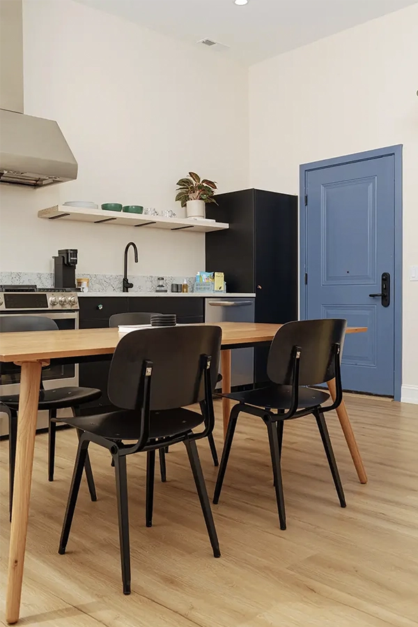Wooden dining table with four black chairs in front of a kitchen counter