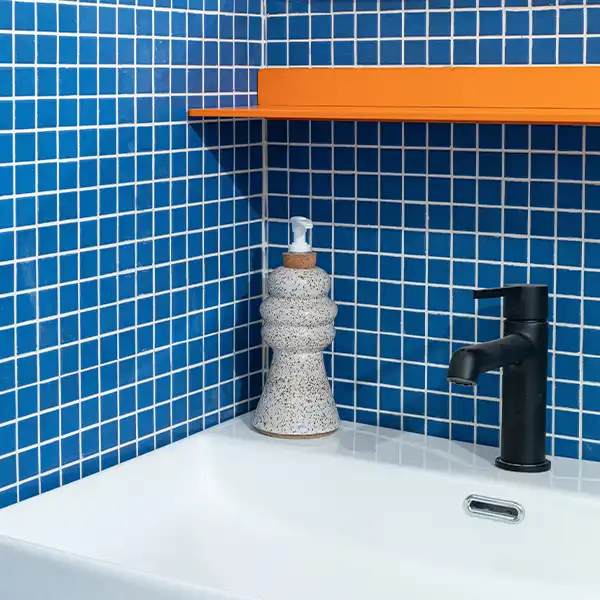 Royal blue tiled bathroom, white sink, and orange fixtures