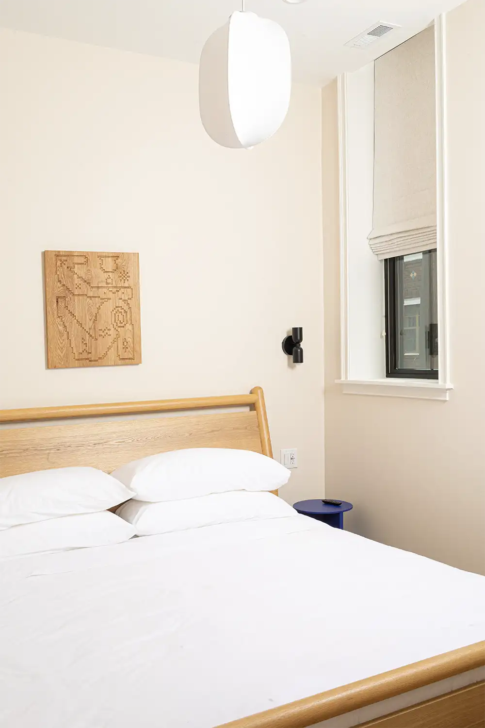 Beige bedroom whit a double bed with white bedding, next to a small window