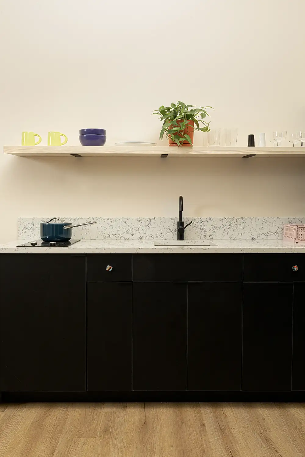 marble kitchen counter with sink and a pot, a beige shelf on top with white plates, purple bowls, yellow mugs and a plant
