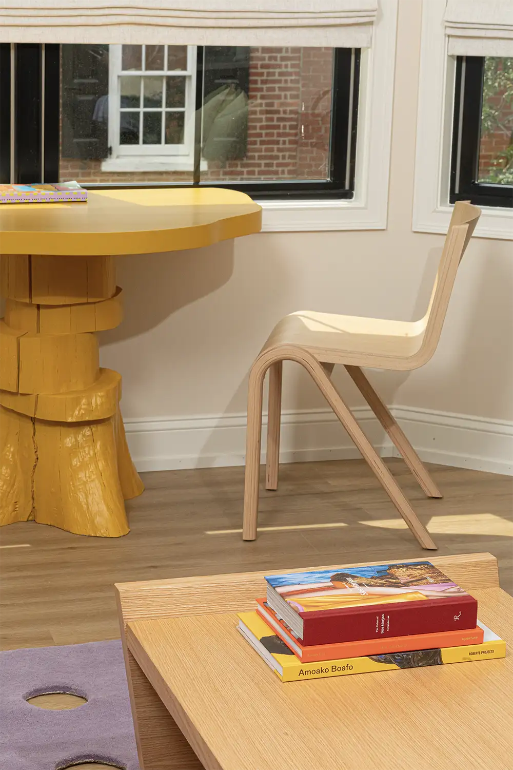 An artistic wooden table painted in yellow whit a light wood chair next to a window