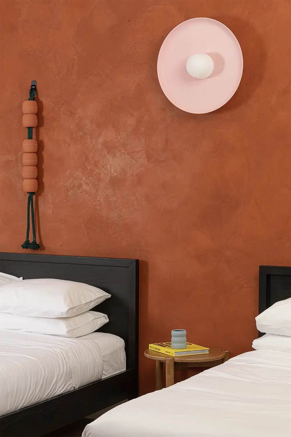 Terracotta wall room with a pink lamp, a black frame bed with white bedding and a light wood nightstand