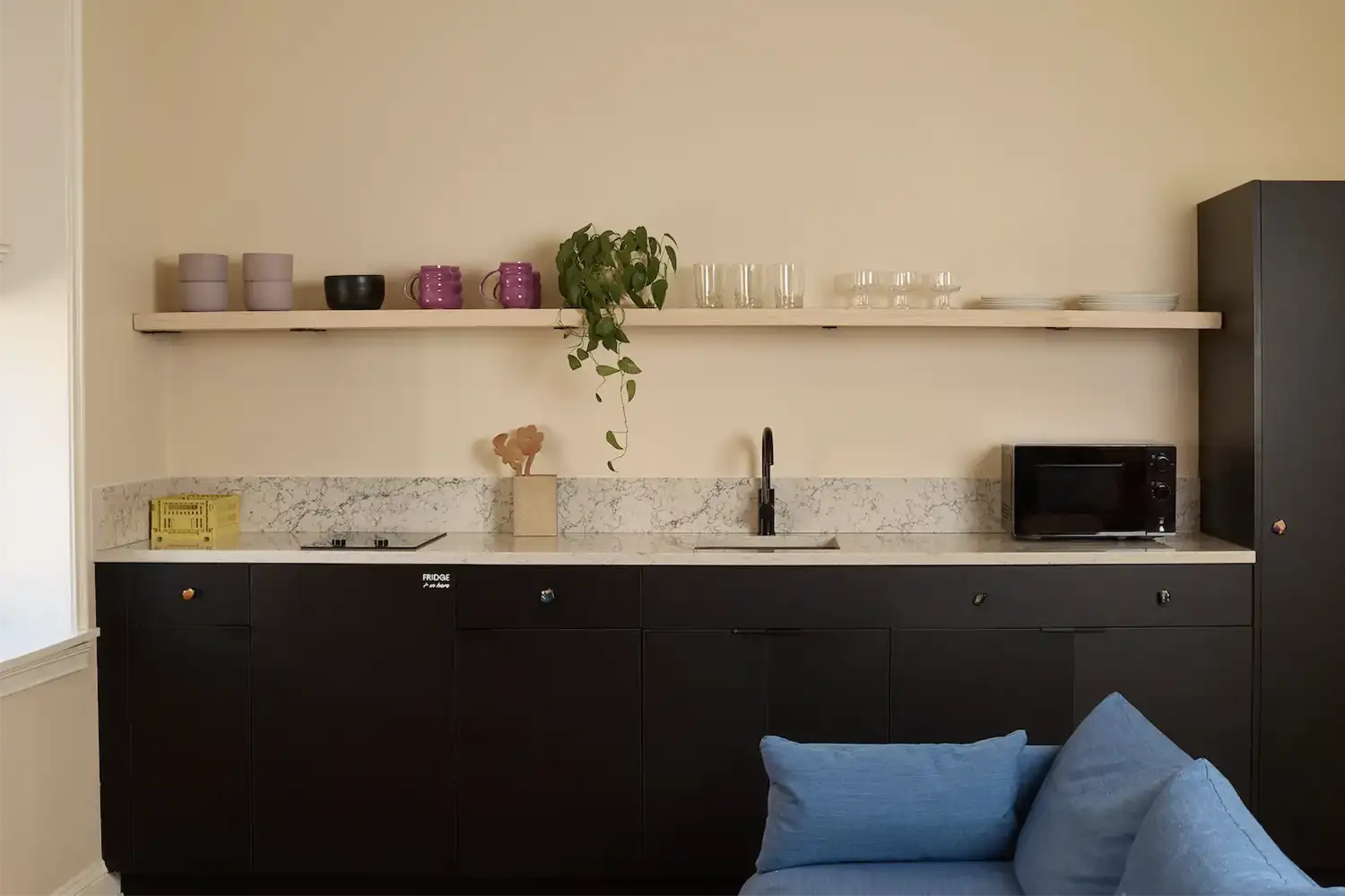 marble kitchen counter with sink and kitchen utensils and a beige shelf on top with white plates, purple mugs, lilac bowls and a plant
