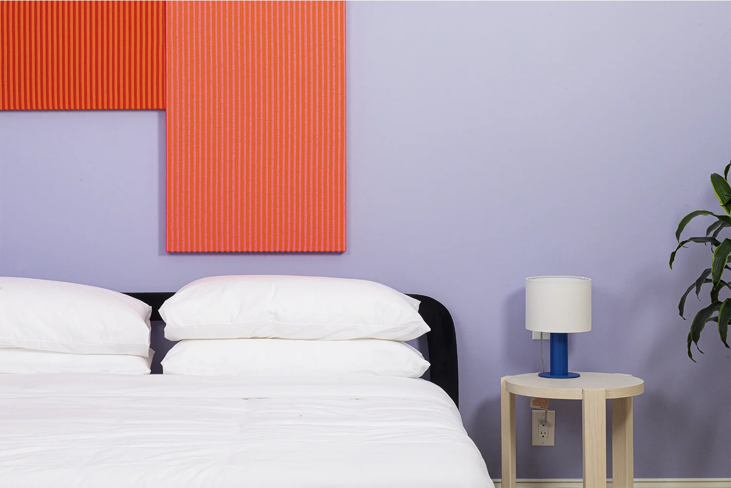 A purple wall bedroom with an artistic red painting on the wall and a double bed beneath next to a light wood nightstand with a blue night lamp