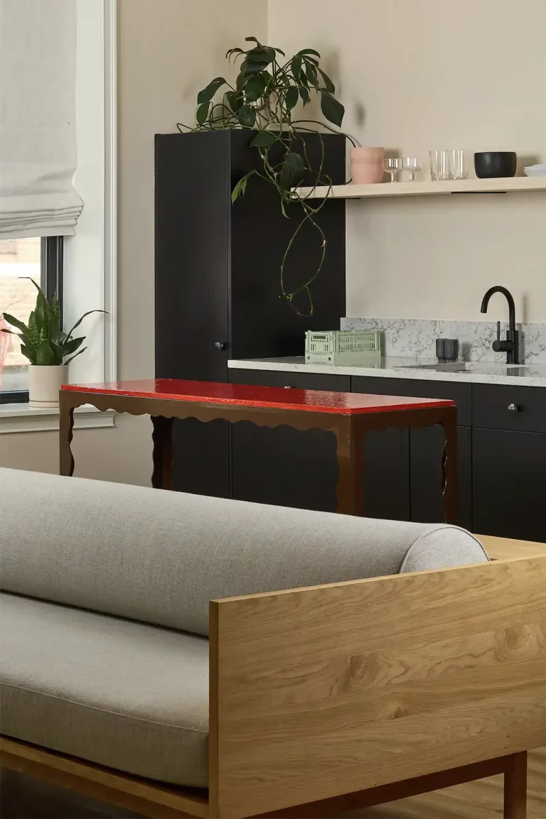 Marble kitchen counter on a side of a medium size window with a wood and red table and the back of a grey sofa