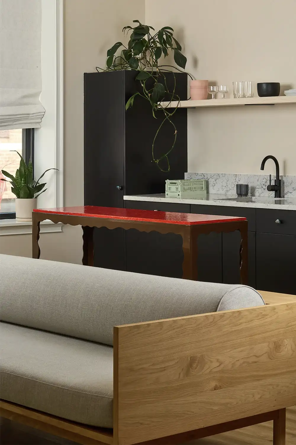 Marble kitchen counter on a side of a medium size window with a wood and red table and the back of a grey sofa