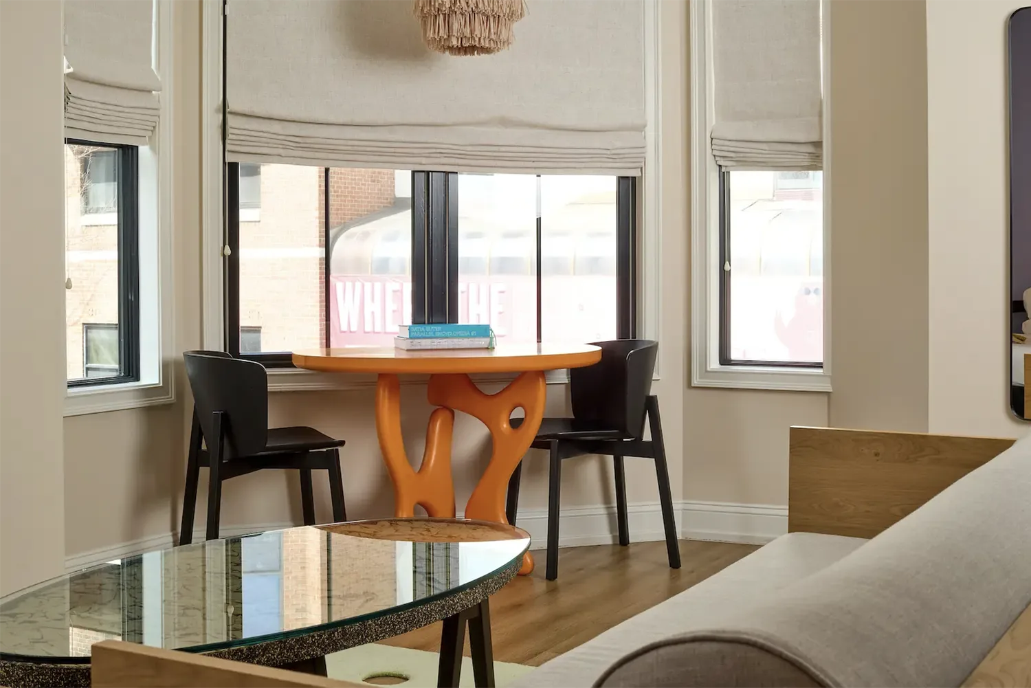 An orange artistic table with two black chairs and books on top next to a window
