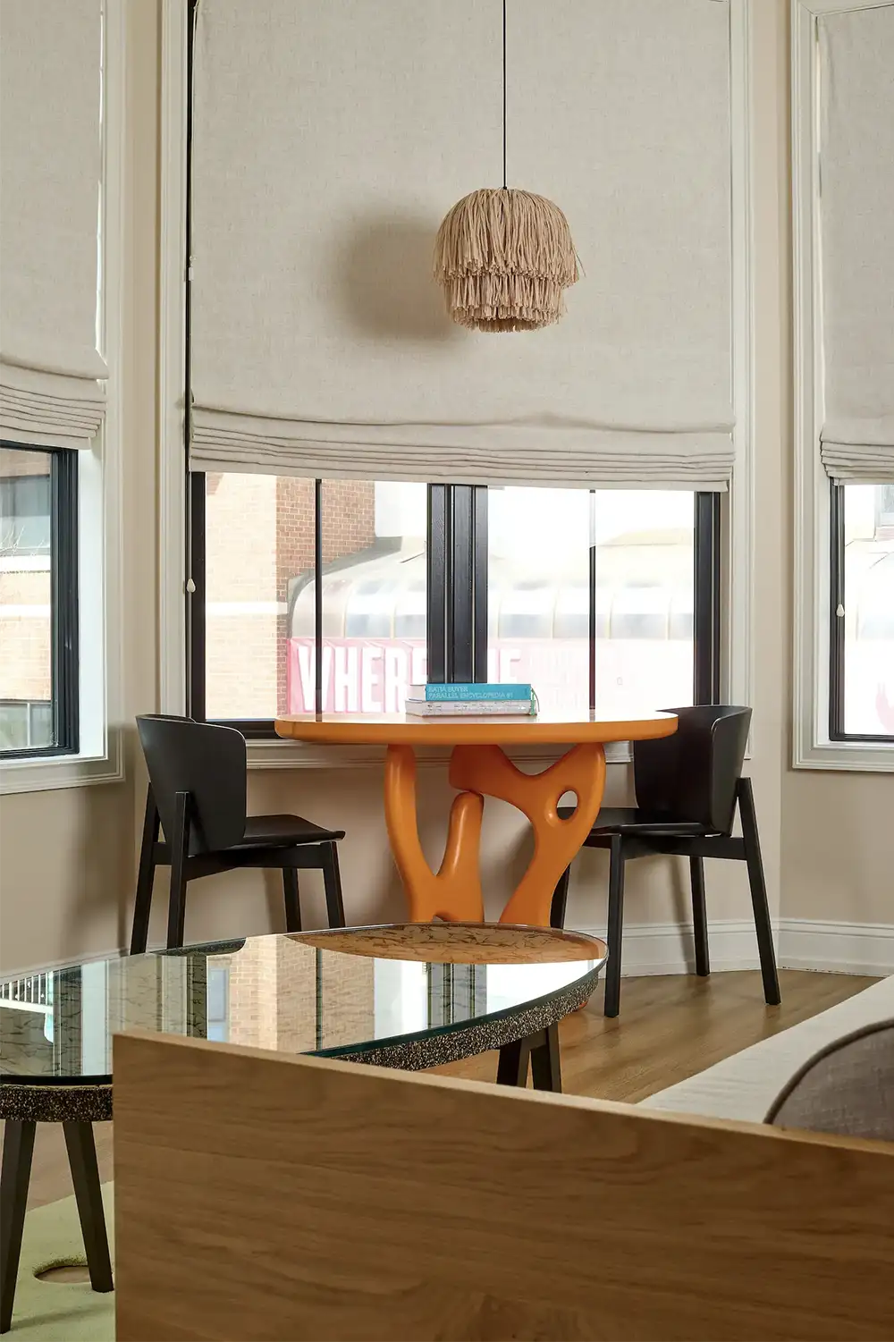 An orange artistic table with two black chairs and books on top next to a window
