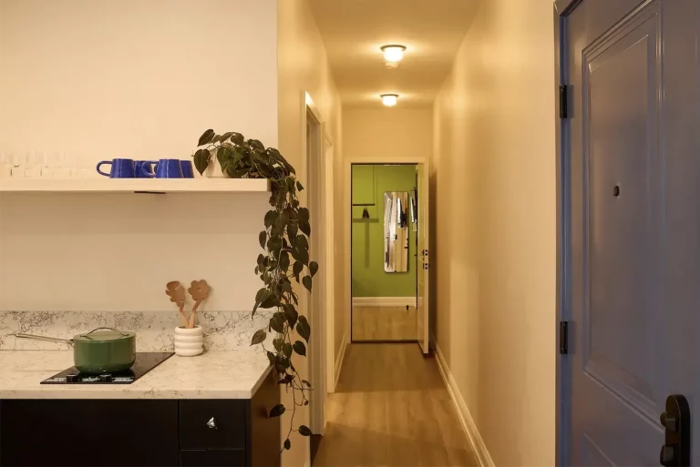 Suite beige hall to the entrance of a room, the corner of a kitchen marble counter and the inside of a purple front door with black handle