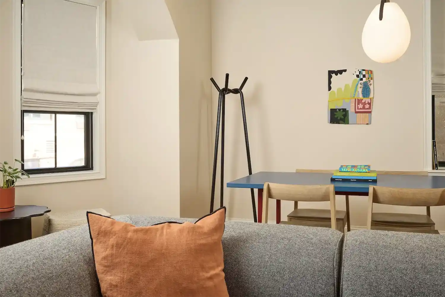 Blue wood table with 4 wood chairs around next to a window, books on top, a hanging lap and the back of a gray sofa