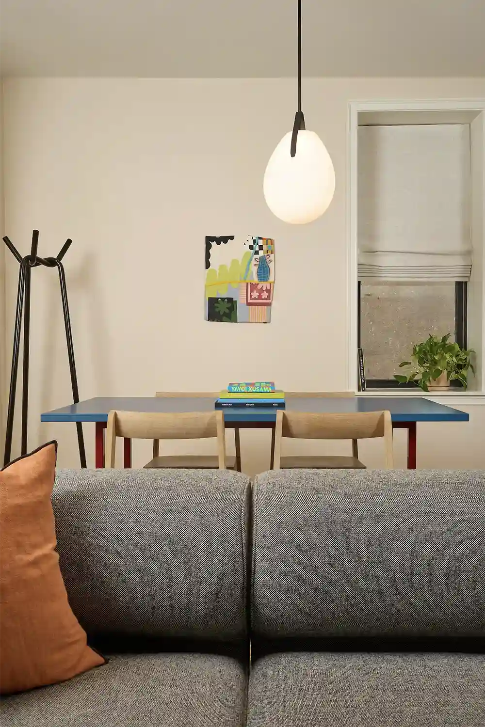 Blue wood table with 4 wood chairs around, books on top and a hanging lap and the back of a gray sofa