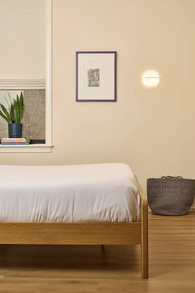 Beige room with a double wood foot bed with white sheets, a purple picture frame