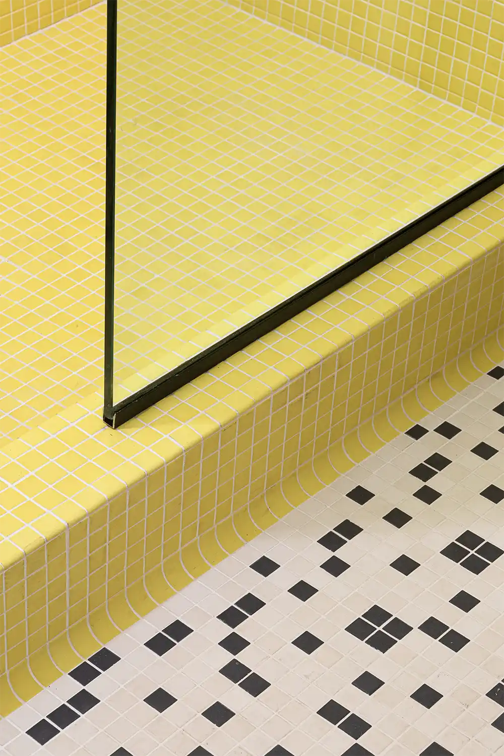 Modern bathroom design with pastel yellow mosaic shower tiles and patterned black-and-white floor tiles, divided by a sleek glass panel.