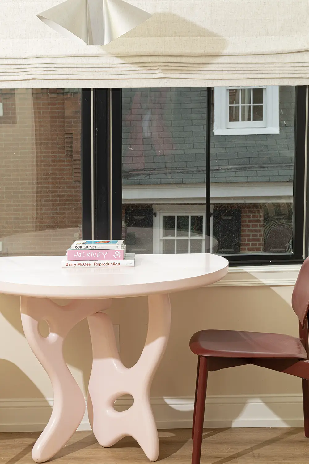 Pink artistic table whit a red wine chair next to a window