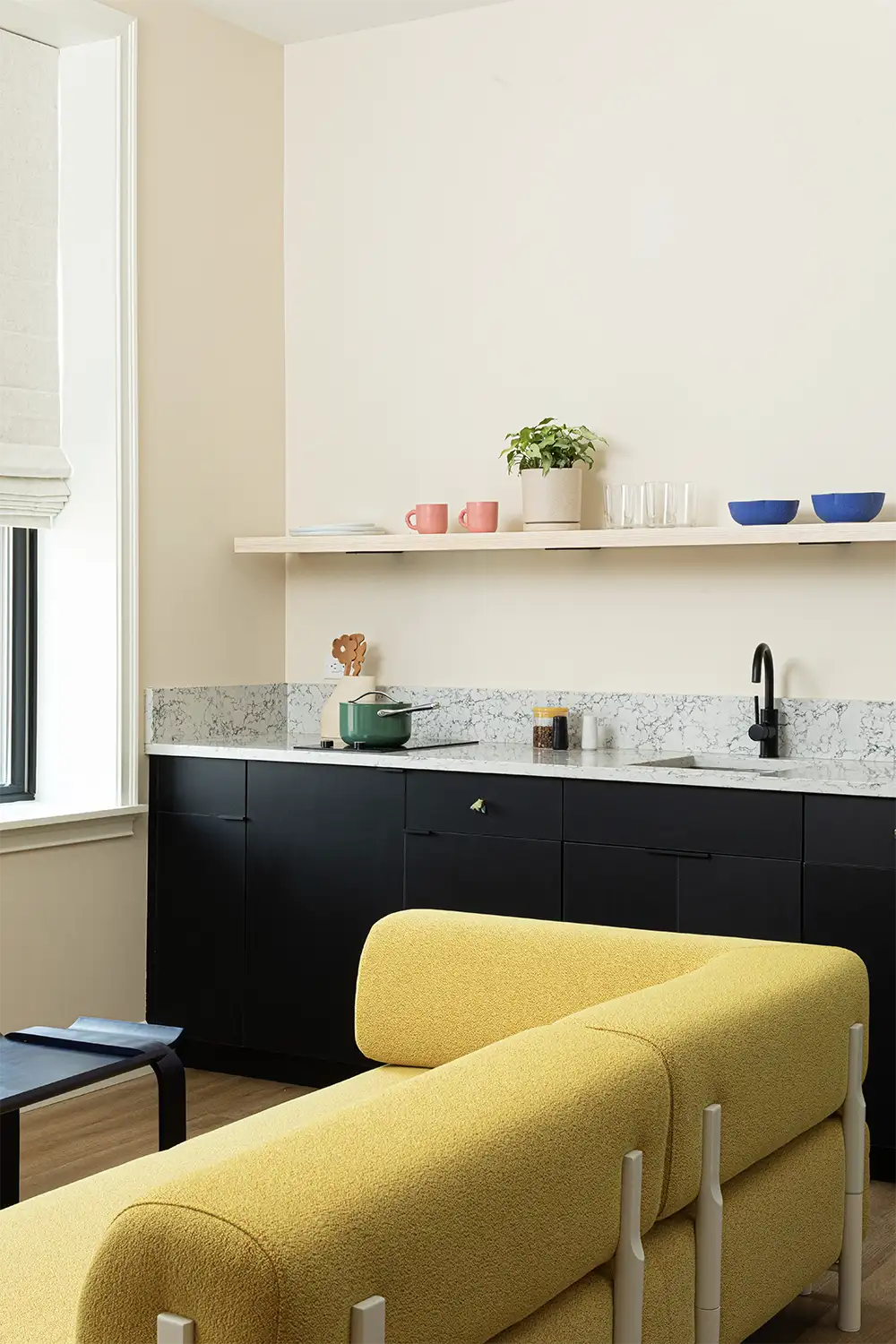yellow sofa with metal legs next to a marble kitchen counter whit a shelf on top holding food crockery