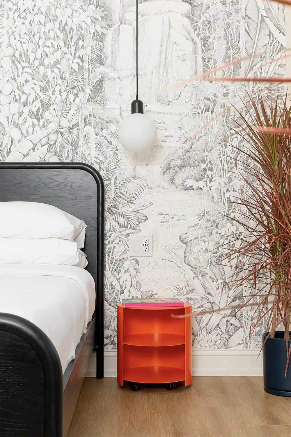 Corner of a room with gray figure wallpaper, an orange nightstand and a big plant
