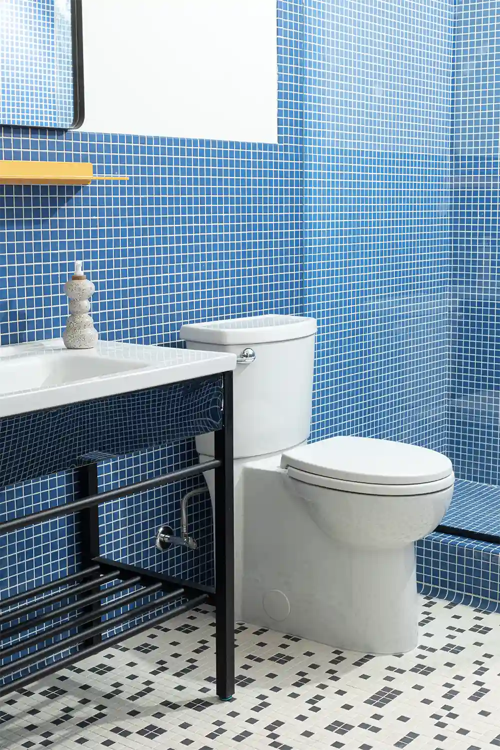 Bathroom with royal blue tiles, a large hanging mirror, a yellow shelf underneath, a white sink with hand soap dispenser, a white toilet, and a glass-enclosed shower.