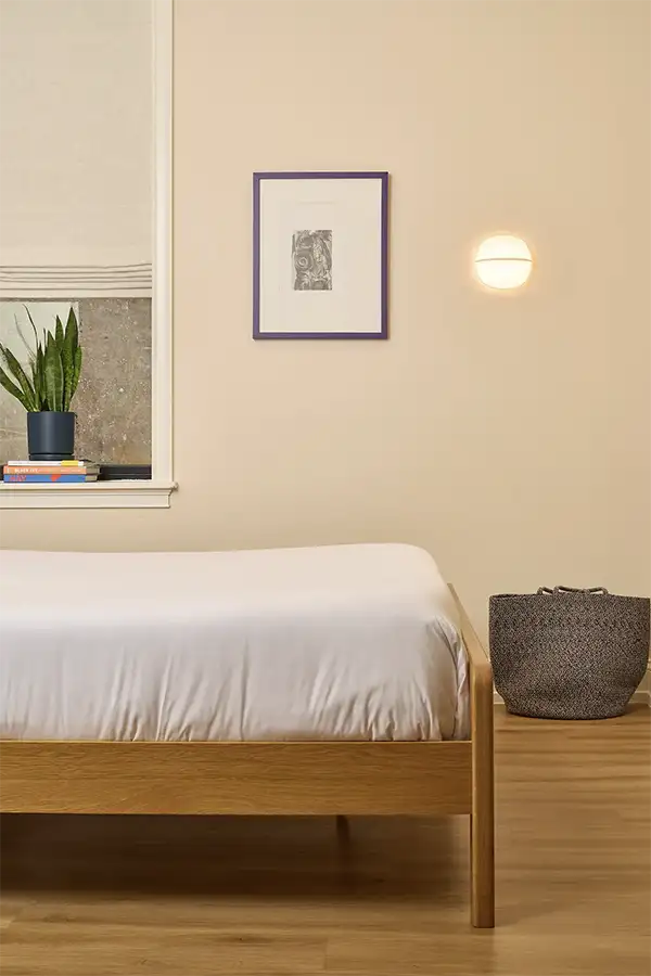 Beige room with a double wood foot bed with white sheets, a purple picture frame