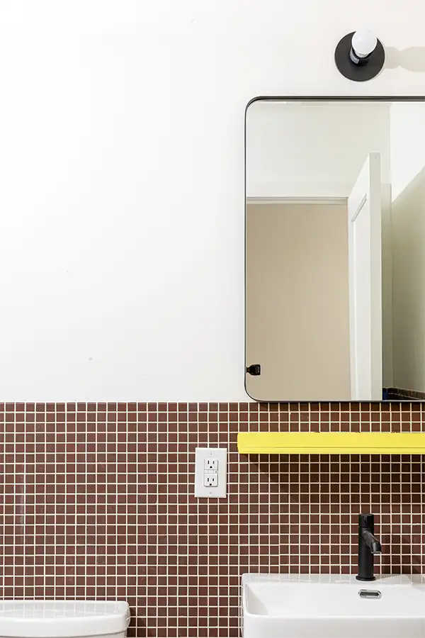 Bathroom with a white sink in front of a brown tiled wall and a mirror