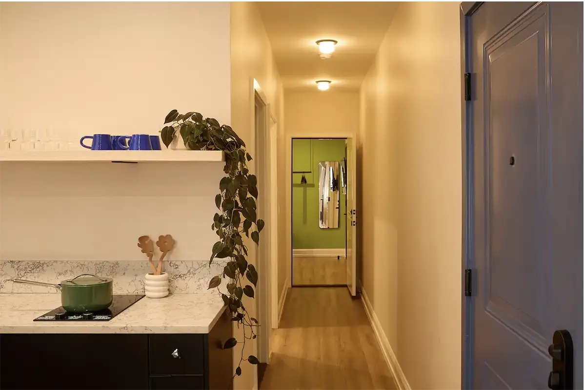 Suite beige hall to the entrance of a room, the corner of a kitchen marble counter and the inside of a purple front door with black handle