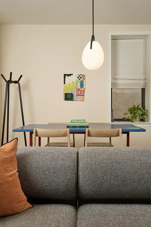 Blue wood table with 4 wood chairs around, books on top and a hanging lap and the back of a gray sofa