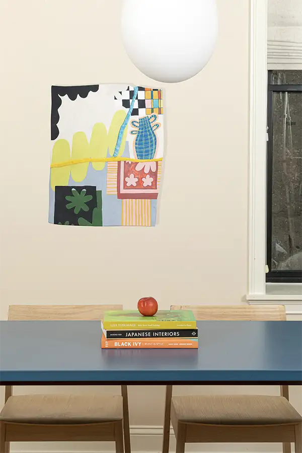 Blue wood table with 2 wood chairs around, books on top and a hanging lap