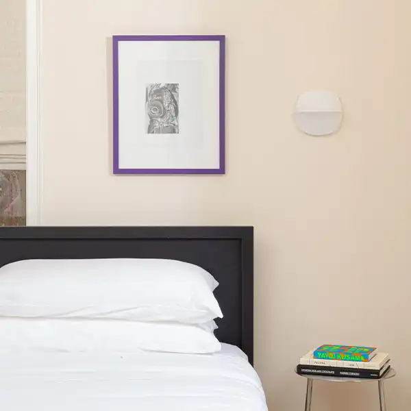 beige room, with a bed with white sheets and a purple framed picture
