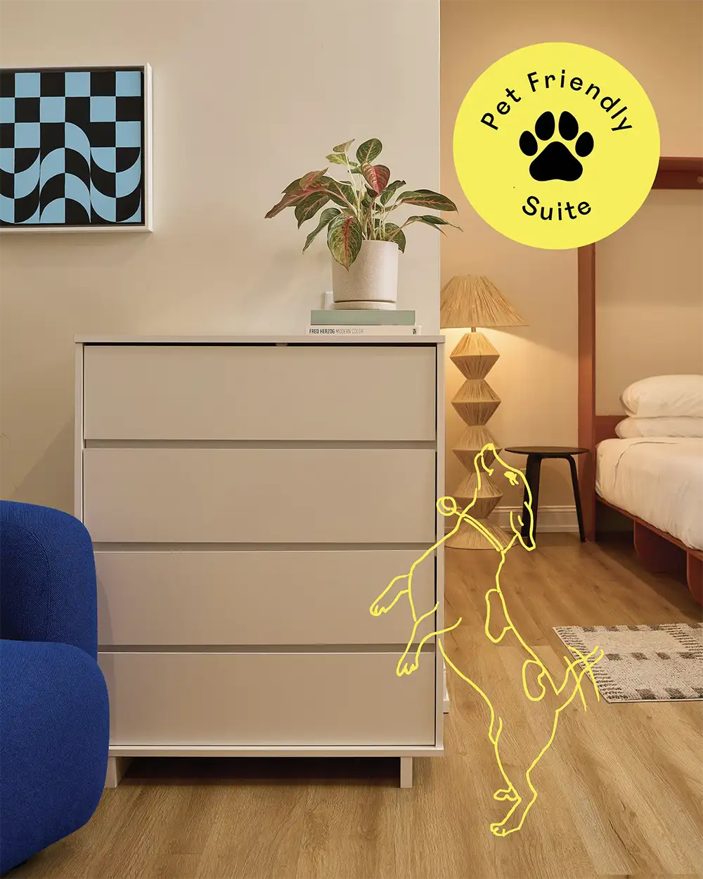 Corner of a room with a blue armchair and a withe chest of drawers with the illustration of a dog and a 