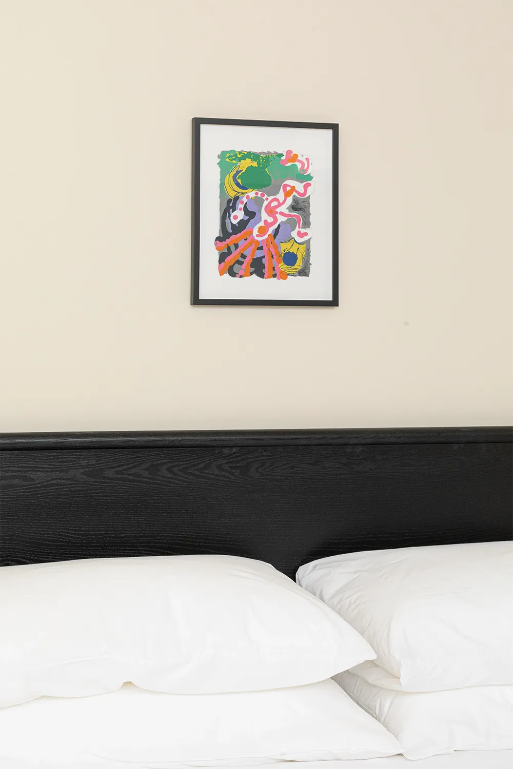 headboard of a black bed against a beige wall with a small colorful painting