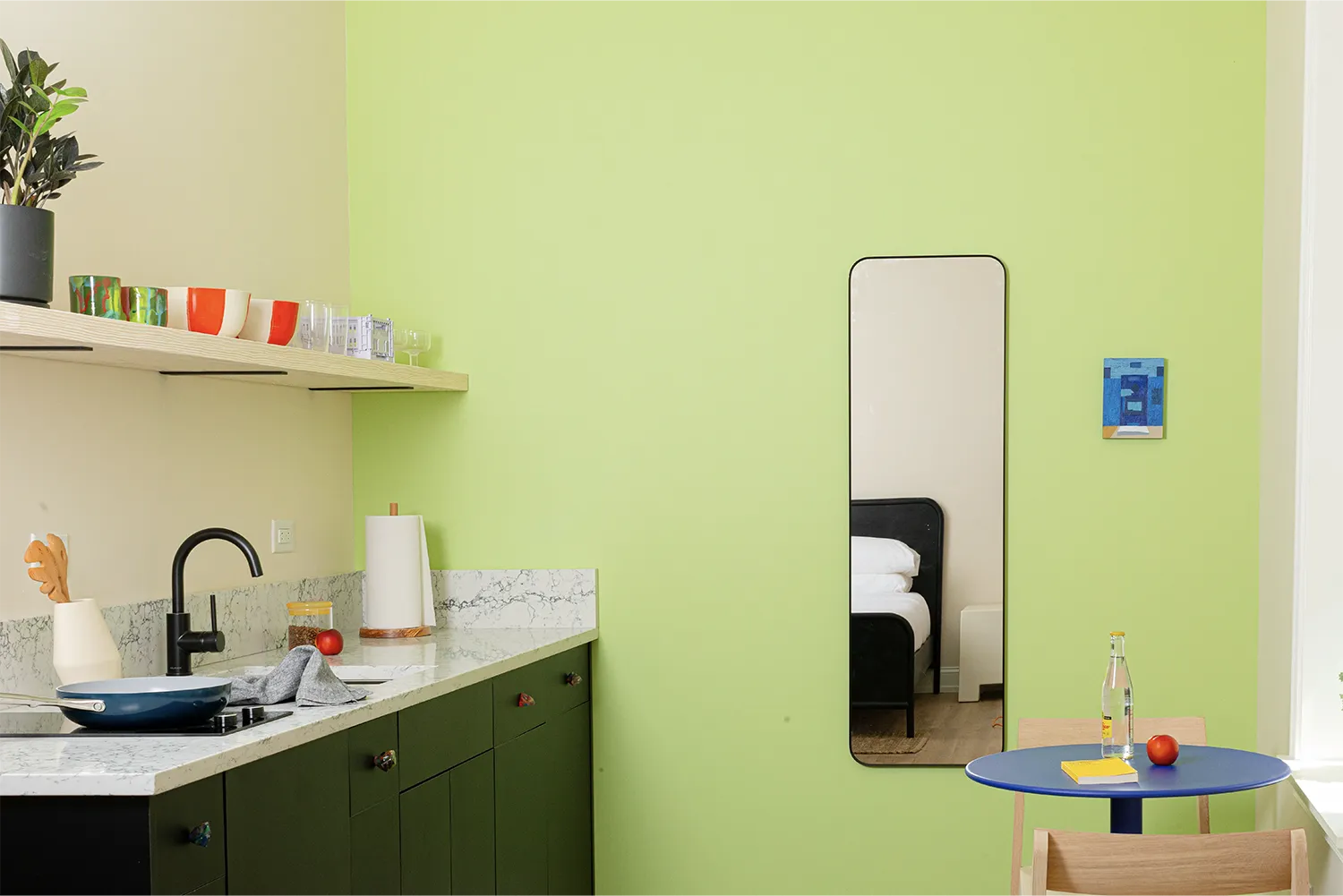 Kitchen counter against a light green wall with a small blue table with two wood chairs and a full-length mirror
