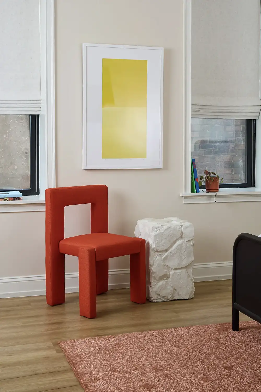 Artistic orange chair against a beige wall with two windows and a stone-like shaped white table