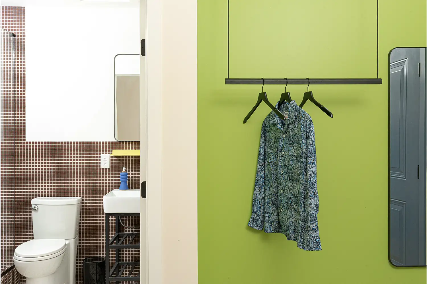 Entrance of a bathroom next to a green wall with a hanging rack with a colorful shirt on it