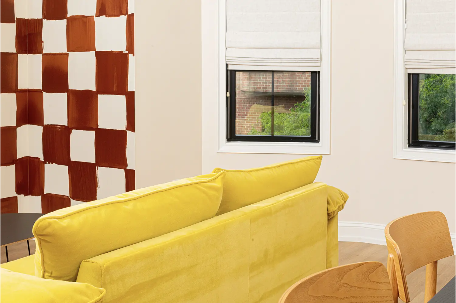 Living room with a yellow sofa, two medium windows and a painted wall with brown squares