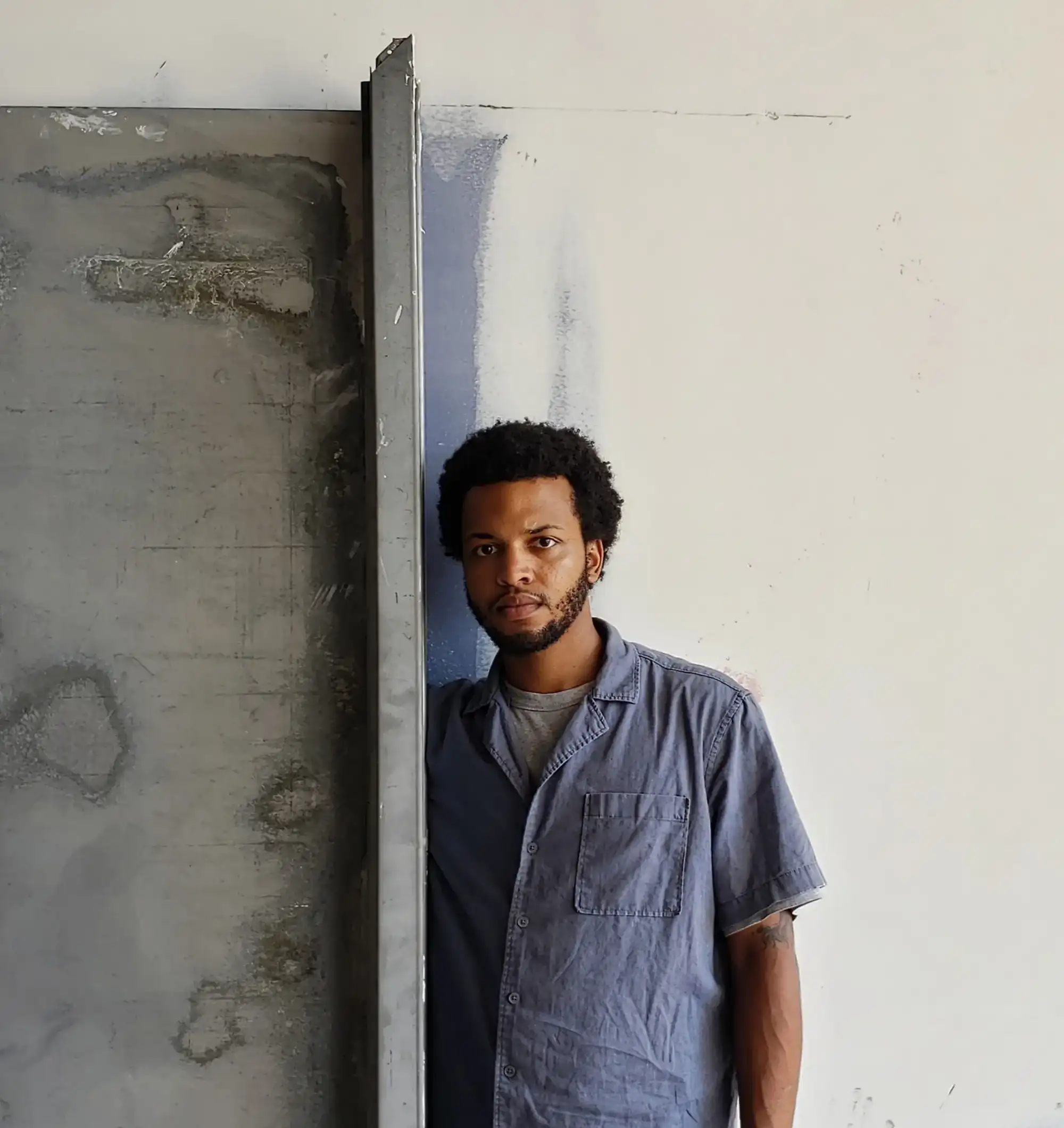 Man in a blue short-sleeved shirt leaning against a cement wall