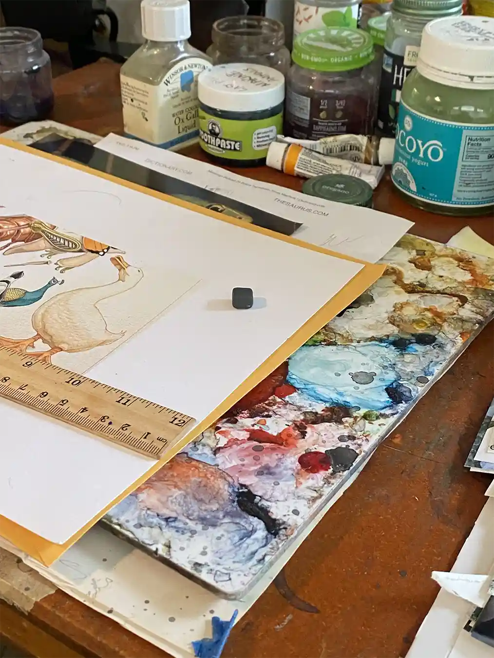 desk full of canvases, brushes and paints