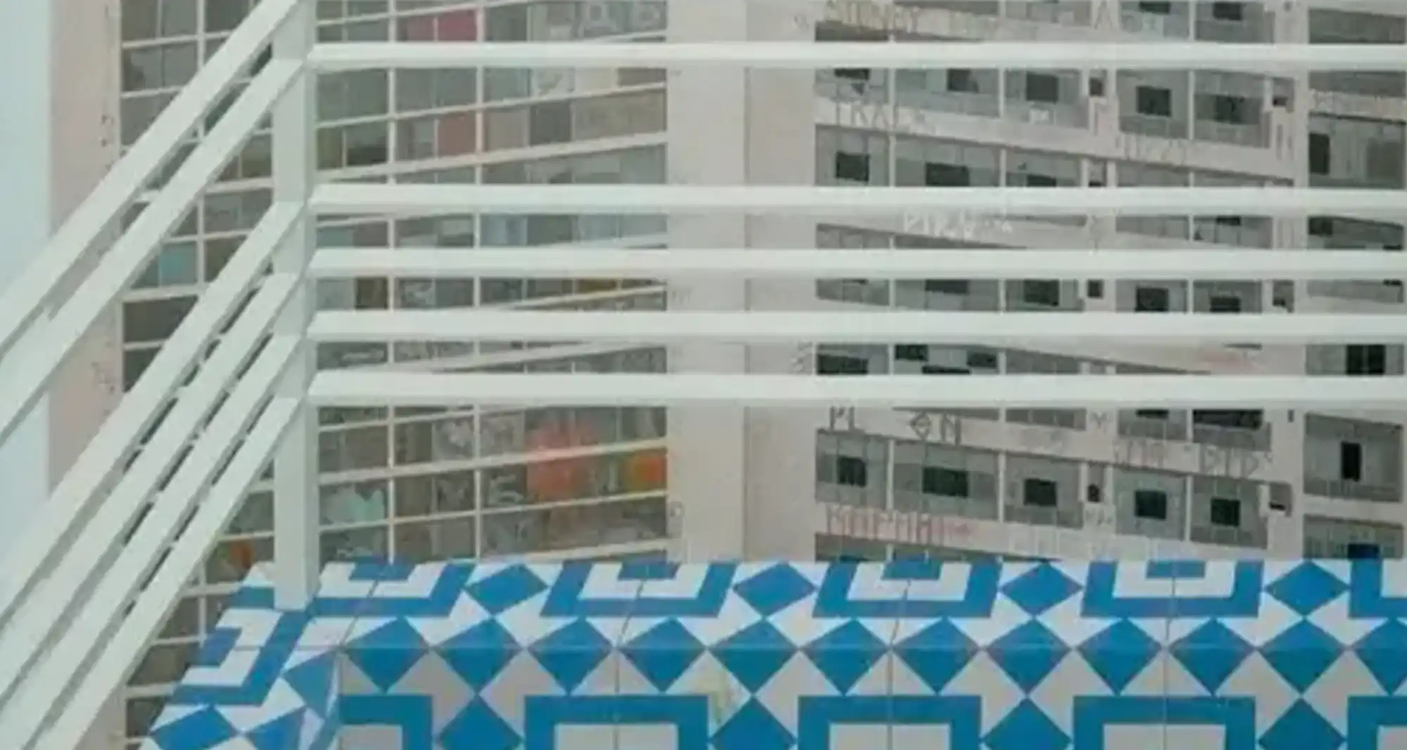 Photograph of some blue tiles with a white fence and a building behind them