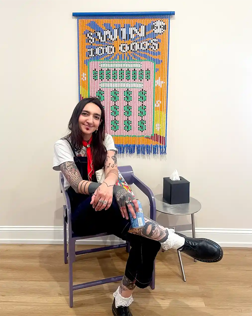 tattooed woman sitting next to a handmade painting