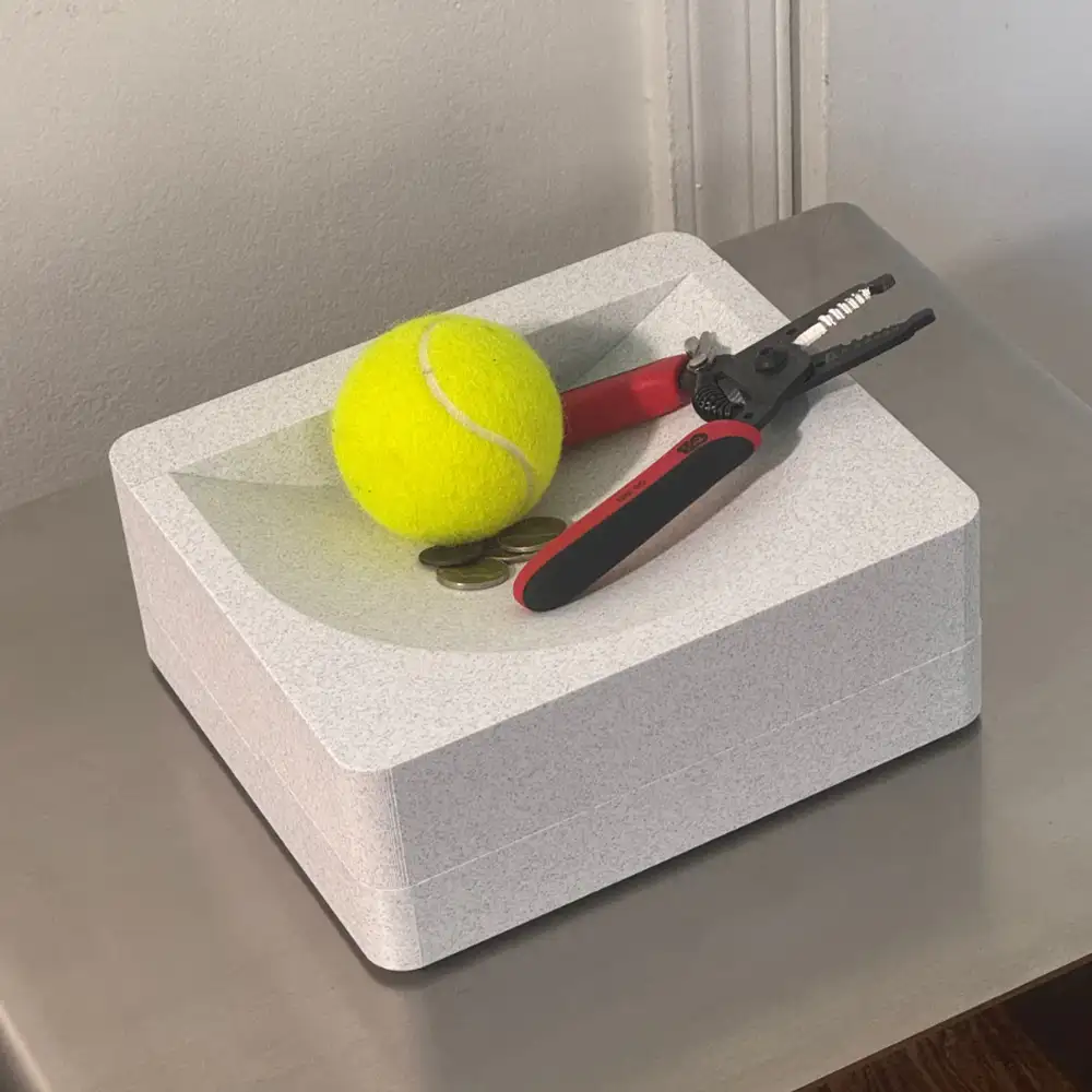 gray sculpture with pliers and a tennis ball on top