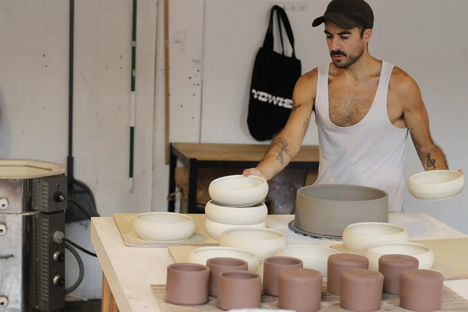 Man with a mustache wearing a sleeveless with t-shirt arranging some clay white bowls