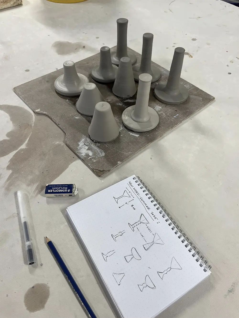 Clay pieces drying on a wooden board next to a notebook with drawings