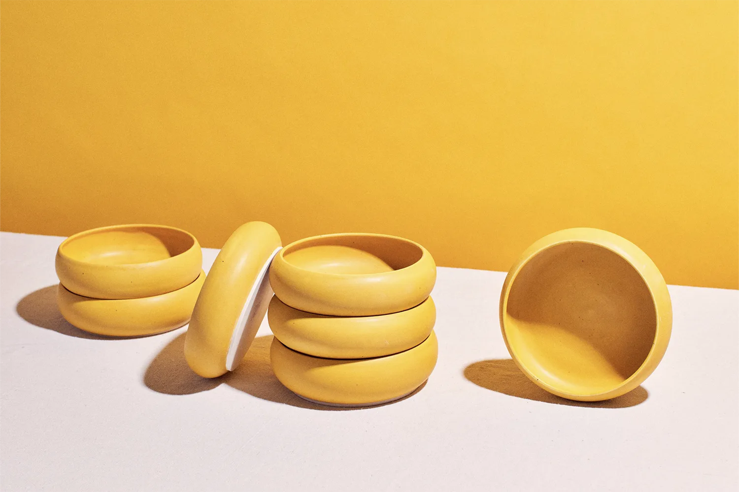 Seven yellow rounded bowls on a white table with yellow background artistically arranged