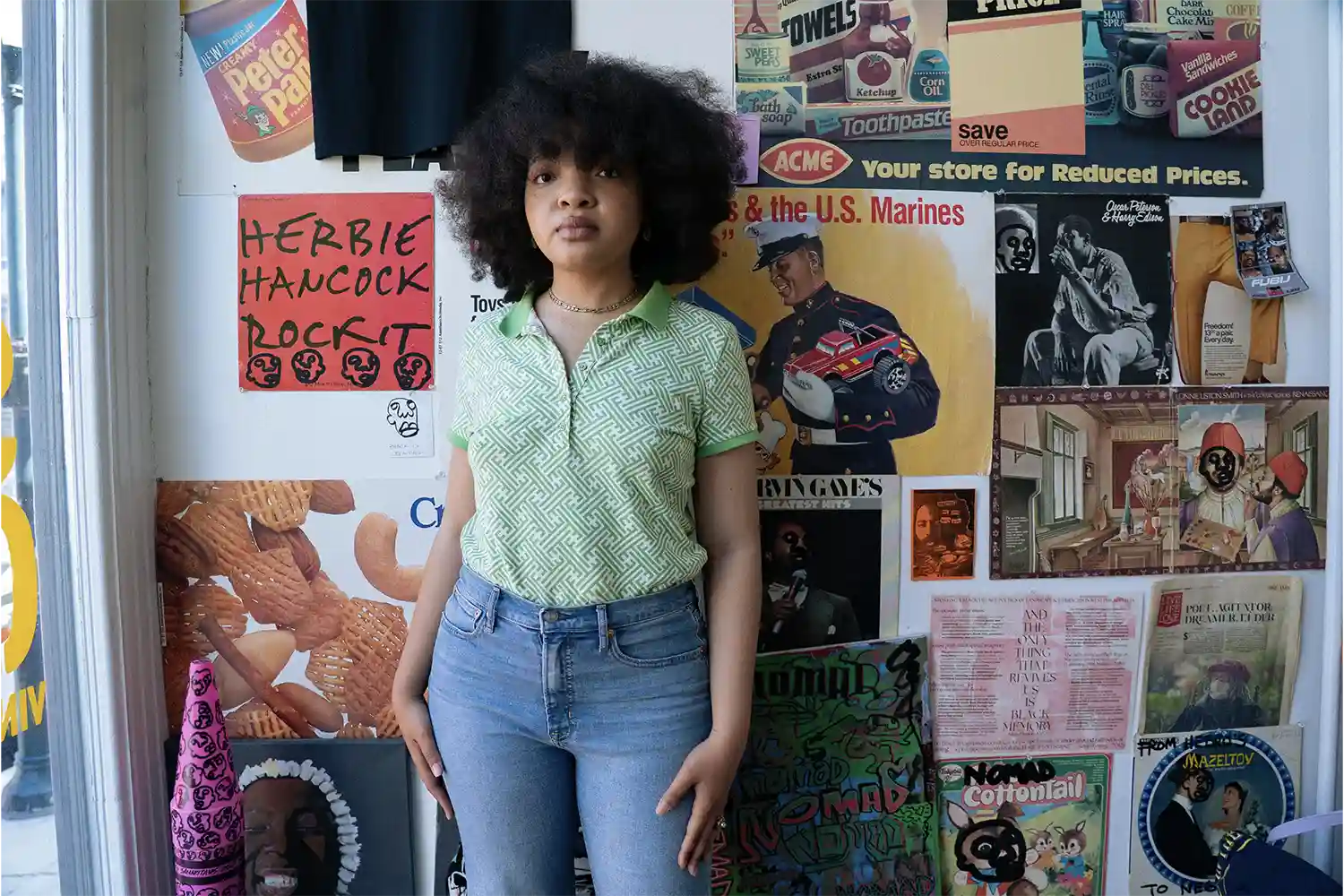Afro young woman wearing a green t-shirt standing in front of a wall full of music posters