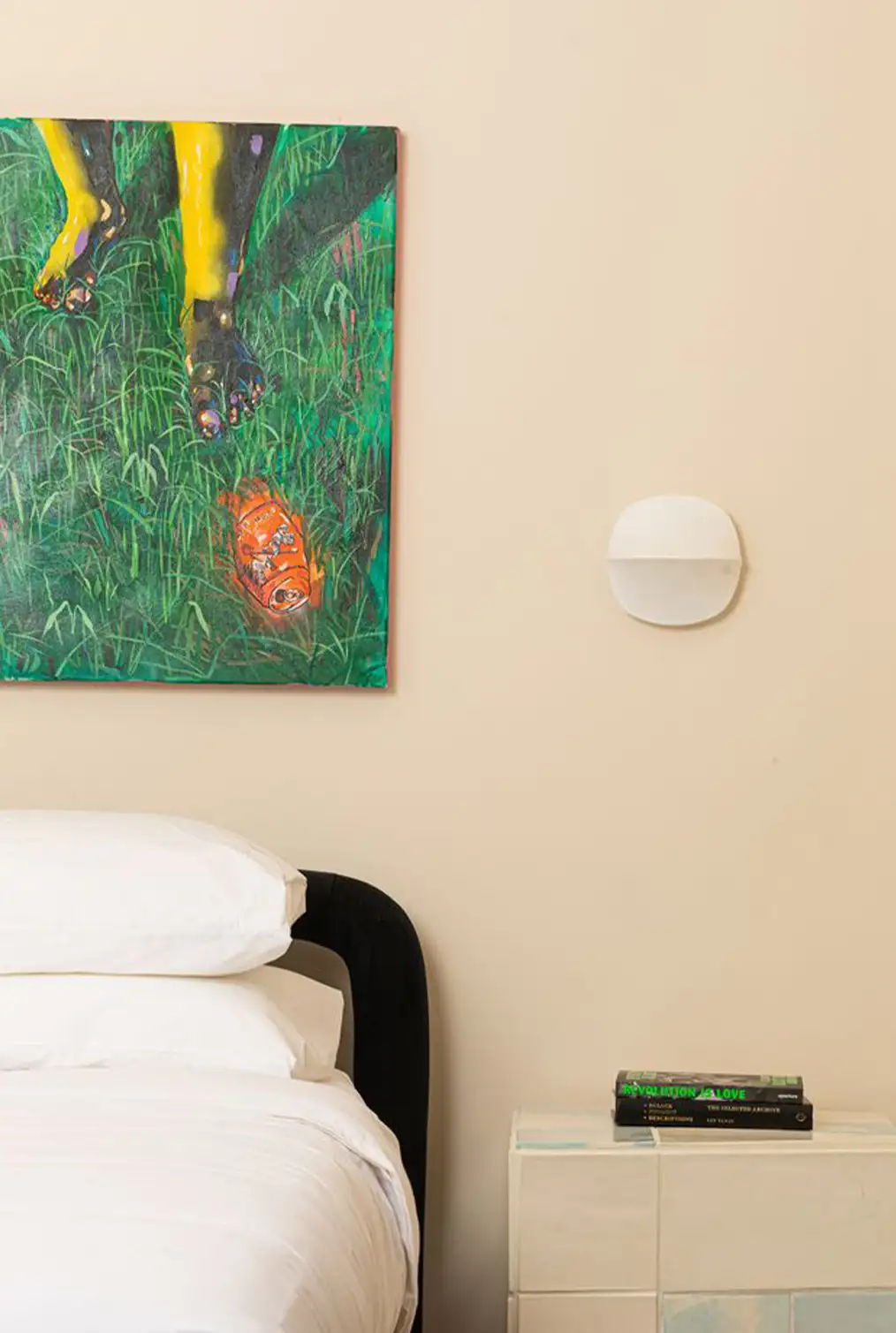 room with a bed with white sheets next to a nightstand with a green painting on it