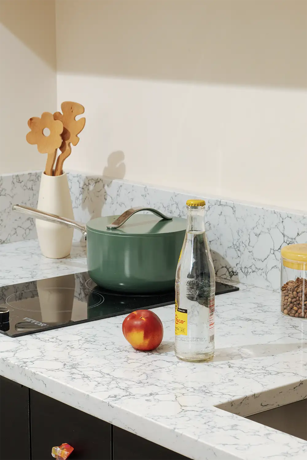 close up of a marble kitchen counter with a pot on an electric stove, a water bottle and a peach placed on top