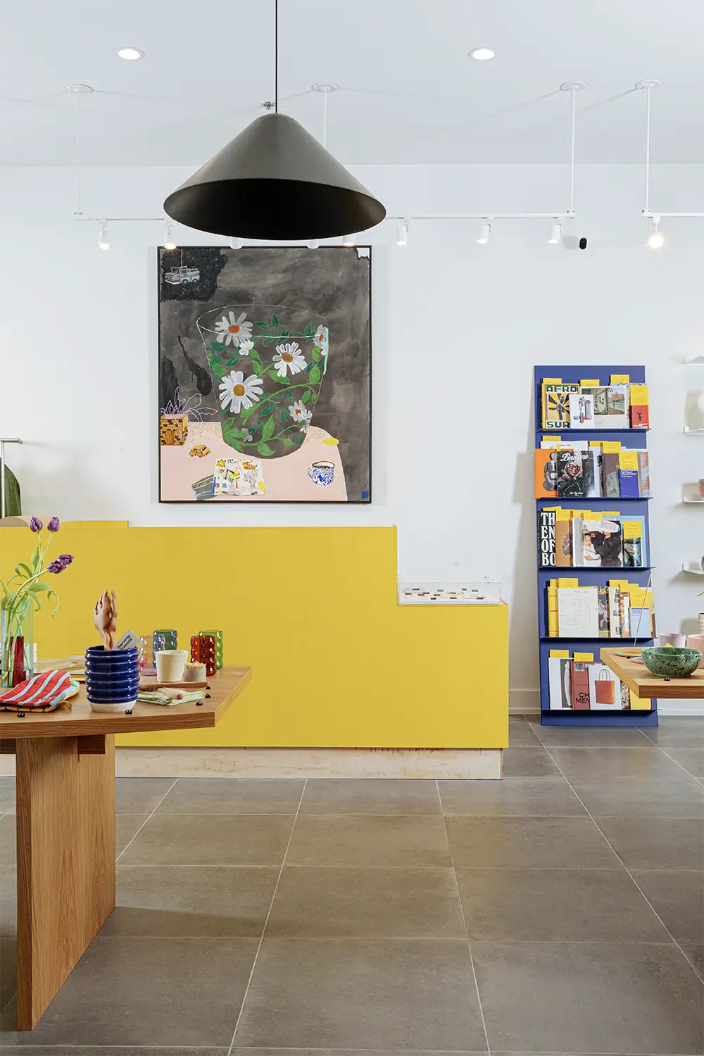 Bright contemporary showroom featuring a bold yellow counter, artistic tableware display, and a vibrant art piece, creating a creative and inviting atmosphere.