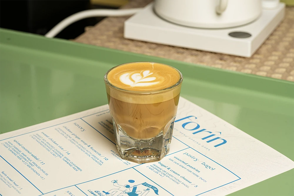 A latte served in a glass on a paper form on a green surface.
