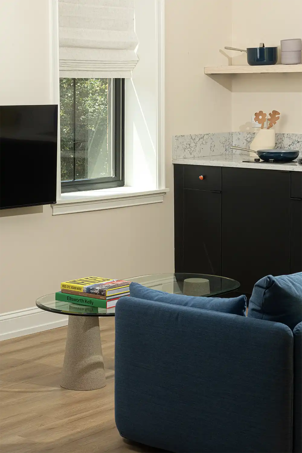Corner of a blue sofa in front of a tv with a glass and stone coffee table