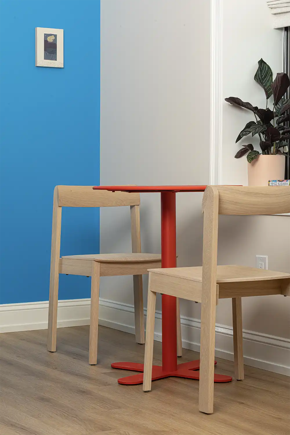 Red artistic table with two wooden chairs next to a small window