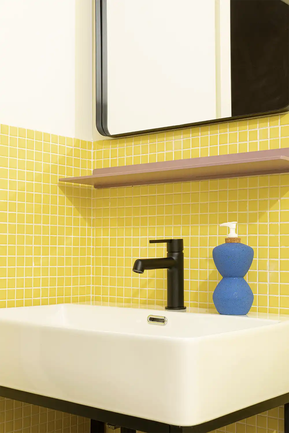 Bathroom sink with yellow tiles wall and a blue hand soap dish on top